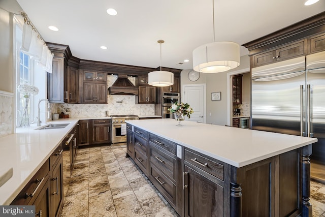 kitchen with high end appliances, light countertops, a sink, dark brown cabinets, and premium range hood