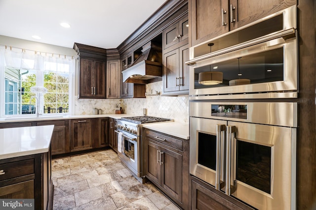 kitchen with light countertops, decorative backsplash, appliances with stainless steel finishes, dark brown cabinets, and premium range hood