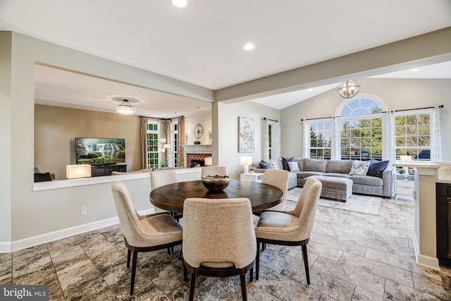 dining room featuring baseboards, stone finish floor, vaulted ceiling, a brick fireplace, and recessed lighting