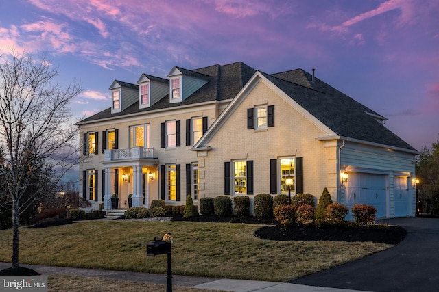 georgian-style home featuring a balcony, a yard, driveway, and brick siding