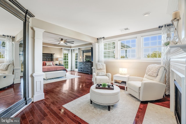 interior space with ceiling fan, wood finished floors, a fireplace with flush hearth, visible vents, and ornate columns