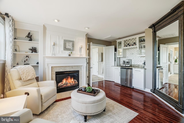 living area with built in features, dark wood-style flooring, recessed lighting, a glass covered fireplace, and a bar