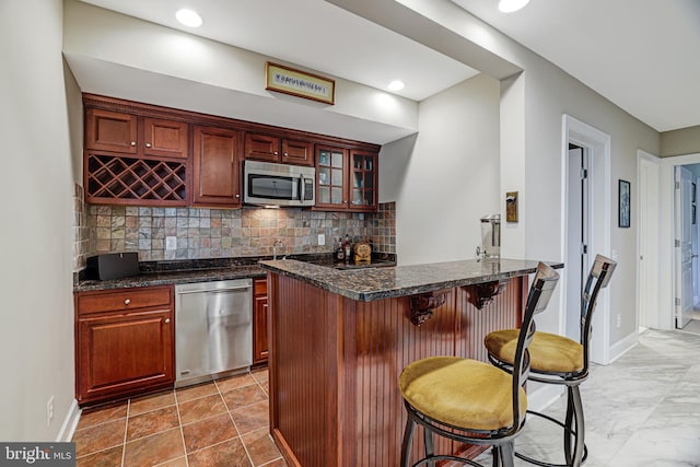 kitchen featuring a breakfast bar area, decorative backsplash, appliances with stainless steel finishes, glass insert cabinets, and baseboards