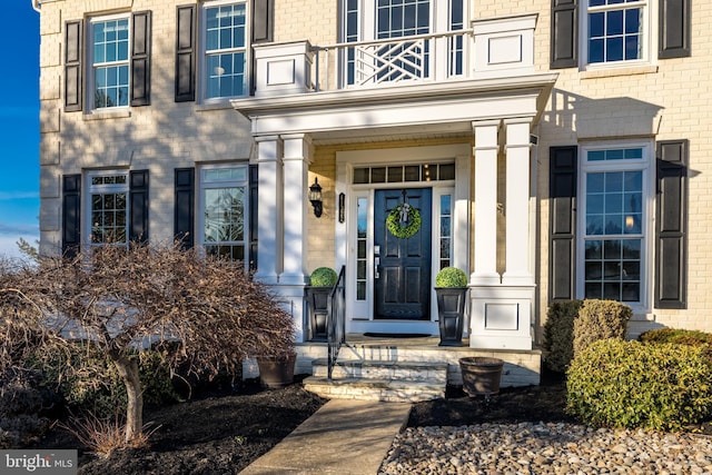 view of exterior entry with brick siding and a balcony