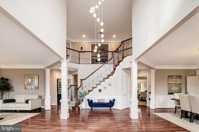 foyer with ornate columns, stairway, wood finished floors, and ornamental molding