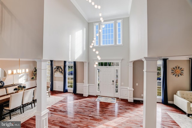 foyer with a wainscoted wall, ornamental molding, wood finished floors, and ornate columns