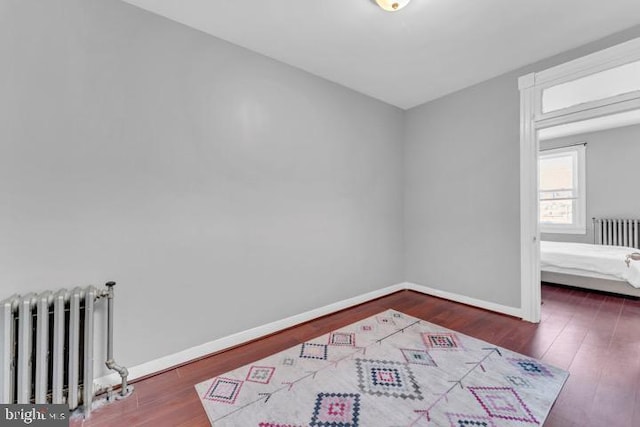 empty room featuring baseboards, dark wood finished floors, and radiator heating unit