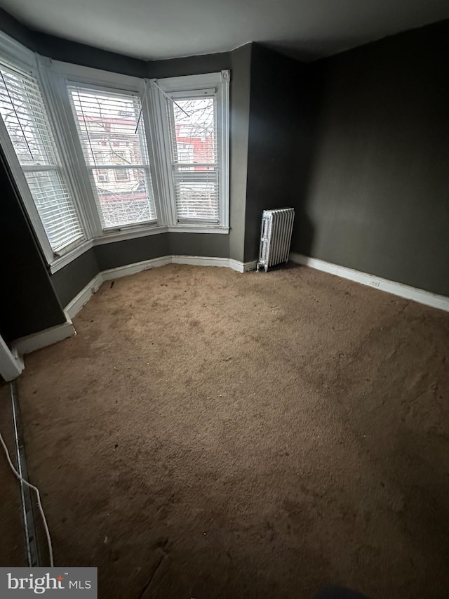 carpeted empty room featuring radiator heating unit and baseboards