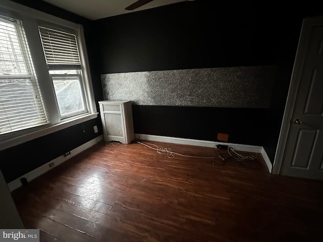 empty room featuring a ceiling fan, dark wood-style flooring, and baseboards