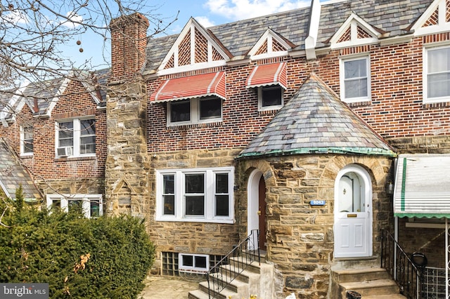 english style home featuring brick siding, a chimney, entry steps, a high end roof, and stone siding