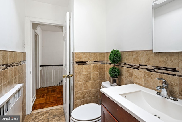 bathroom featuring a wainscoted wall, tile walls, radiator, toilet, and vanity