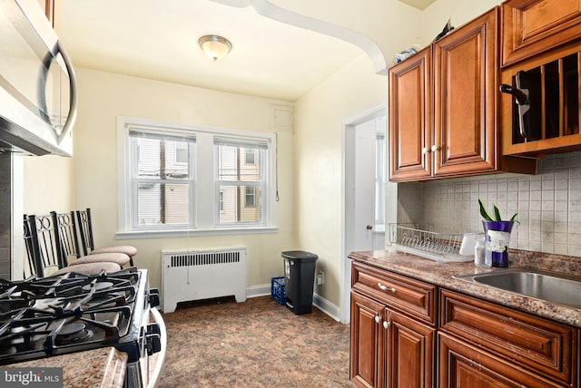 kitchen featuring arched walkways, stainless steel appliances, baseboards, decorative backsplash, and radiator