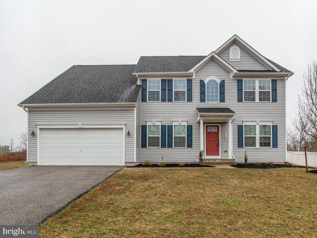 colonial inspired home featuring a garage, driveway, a shingled roof, and a front yard