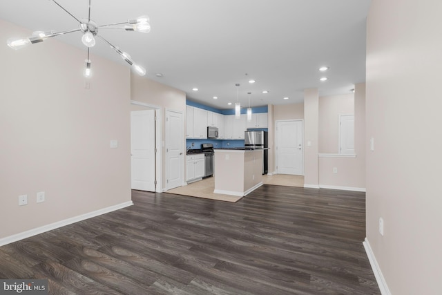 kitchen with wood finished floors, a kitchen island, white cabinetry, appliances with stainless steel finishes, and dark countertops