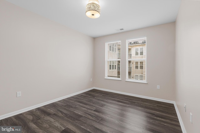 empty room featuring dark wood-style floors, visible vents, and baseboards