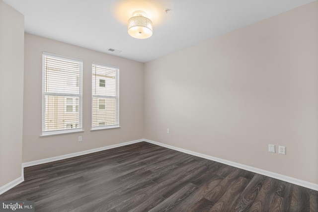 unfurnished room featuring dark wood-style flooring, visible vents, and baseboards