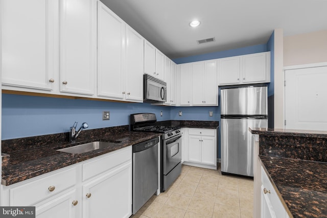 kitchen with light tile patterned floors, stainless steel appliances, a sink, white cabinetry, and dark stone countertops