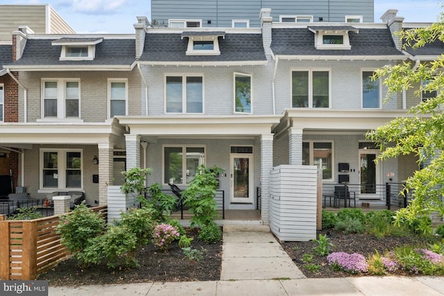 townhome / multi-family property featuring covered porch, brick siding, mansard roof, and a shingled roof
