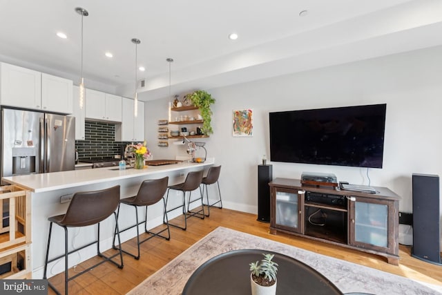kitchen featuring a kitchen breakfast bar, backsplash, white cabinets, light wood finished floors, and stainless steel fridge