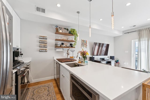 kitchen with white cabinets, appliances with stainless steel finishes, a sink, light wood-type flooring, and visible vents