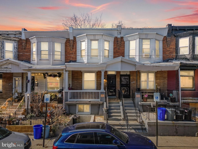 multi unit property featuring covered porch, stairs, and brick siding