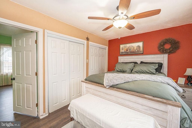 bedroom with dark wood-style floors, ceiling fan, and two closets