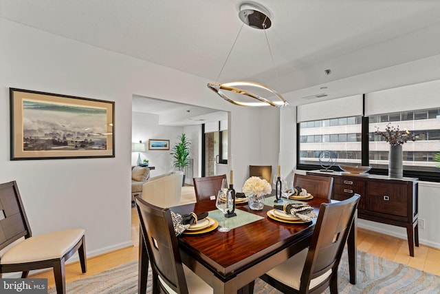 dining space featuring light wood-style floors, a chandelier, visible vents, and baseboards