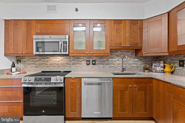 kitchen featuring visible vents, backsplash, appliances with stainless steel finishes, glass insert cabinets, and a sink