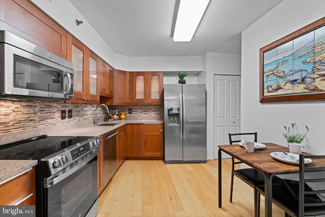 kitchen featuring a sink, light countertops, appliances with stainless steel finishes, brown cabinets, and glass insert cabinets