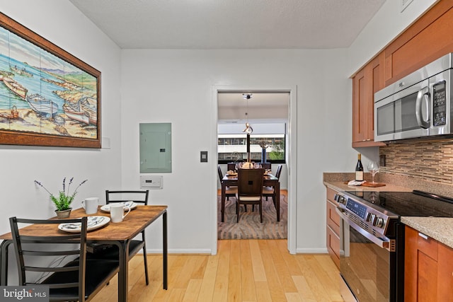 kitchen featuring stainless steel appliances, light wood-type flooring, electric panel, decorative backsplash, and brown cabinetry