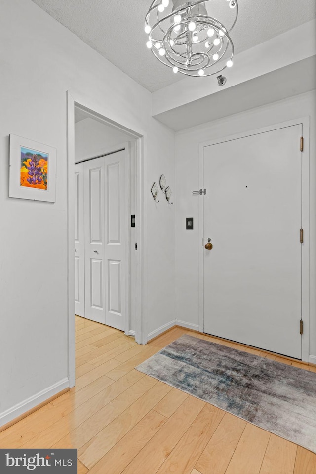 foyer with baseboards, a textured ceiling, an inviting chandelier, and wood finished floors