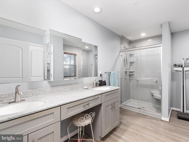 full bath with wood finished floors, a sink, a shower stall, and double vanity