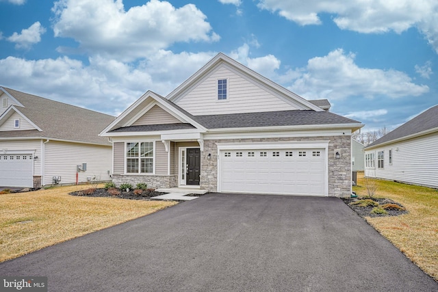 view of front of property featuring driveway, roof with shingles, stone siding, and a front yard