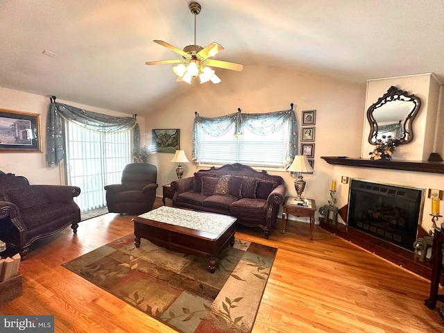 living room with a ceiling fan, lofted ceiling, a fireplace, and wood finished floors