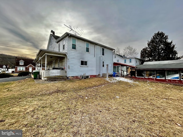 view of side of home featuring a porch, a lawn, and a chimney