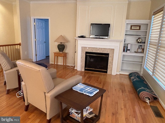 living area with visible vents, built in shelves, ornamental molding, a fireplace, and wood-type flooring