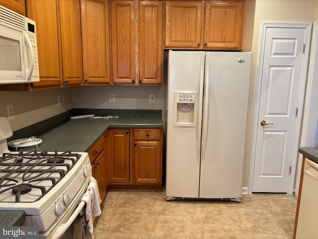 kitchen with white appliances, brown cabinetry, and dark countertops