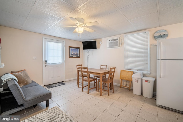 dining area with a ceiling fan, a paneled ceiling, a wall unit AC, and light tile patterned floors