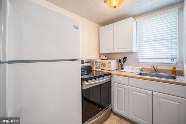 kitchen with light tile patterned floors, white cabinets, a sink, white appliances, and a drop ceiling