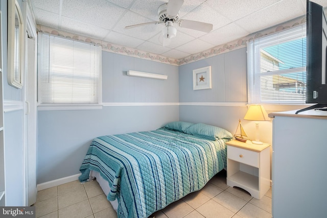 bedroom with a ceiling fan, a drop ceiling, baseboards, and tile patterned floors