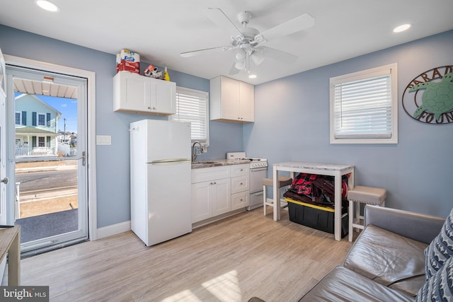 kitchen with white appliances, light wood finished floors, ceiling fan, white cabinetry, and a sink