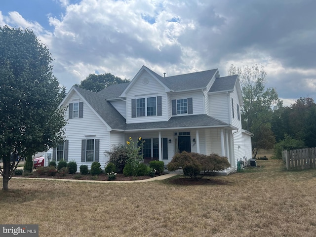 traditional-style home with covered porch, roof with shingles, fence, and a front yard