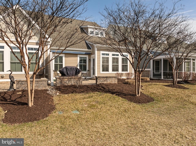 rear view of property featuring a shingled roof, a sunroom, a lawn, and a patio