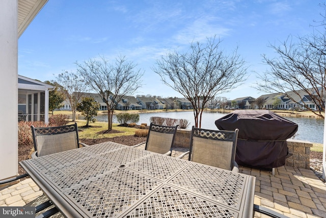 view of patio with grilling area, outdoor dining area, a water view, and a residential view