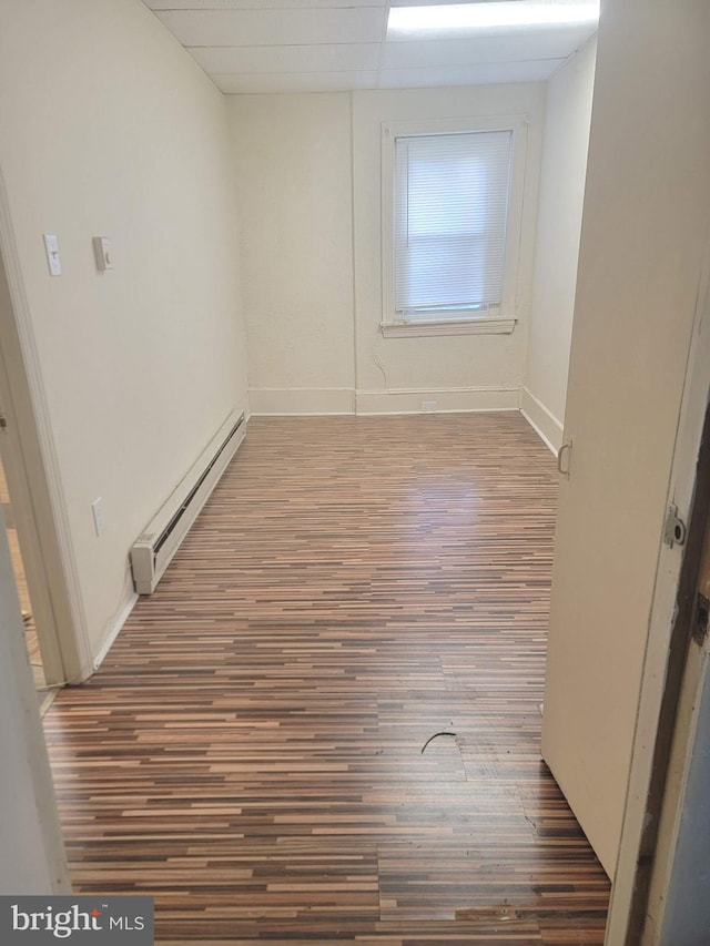 spare room featuring a baseboard radiator, a drop ceiling, baseboards, and wood finished floors