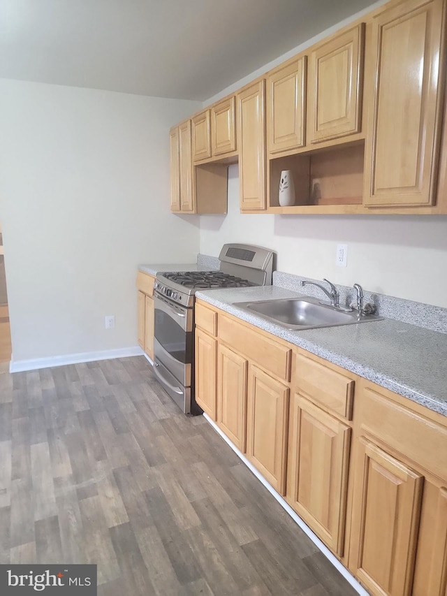 kitchen with stainless steel range with gas cooktop, dark wood-type flooring, light countertops, light brown cabinets, and a sink