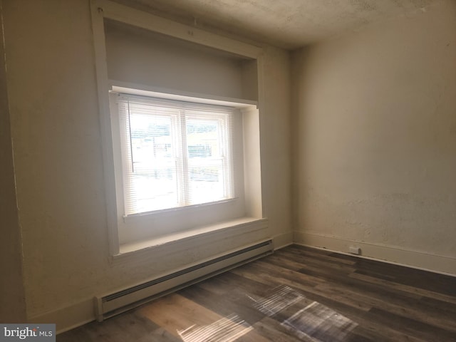 unfurnished room featuring a baseboard heating unit, dark wood-type flooring, and baseboards