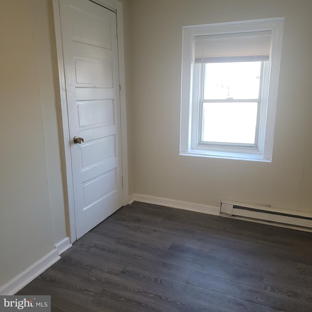 empty room featuring a baseboard heating unit, baseboards, and dark wood-style floors