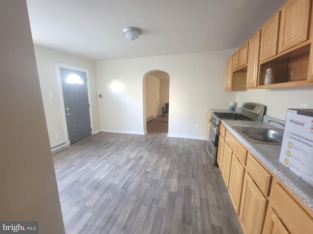 kitchen featuring arched walkways, wood finished floors, baseboard heating, stainless steel range with gas cooktop, and a sink