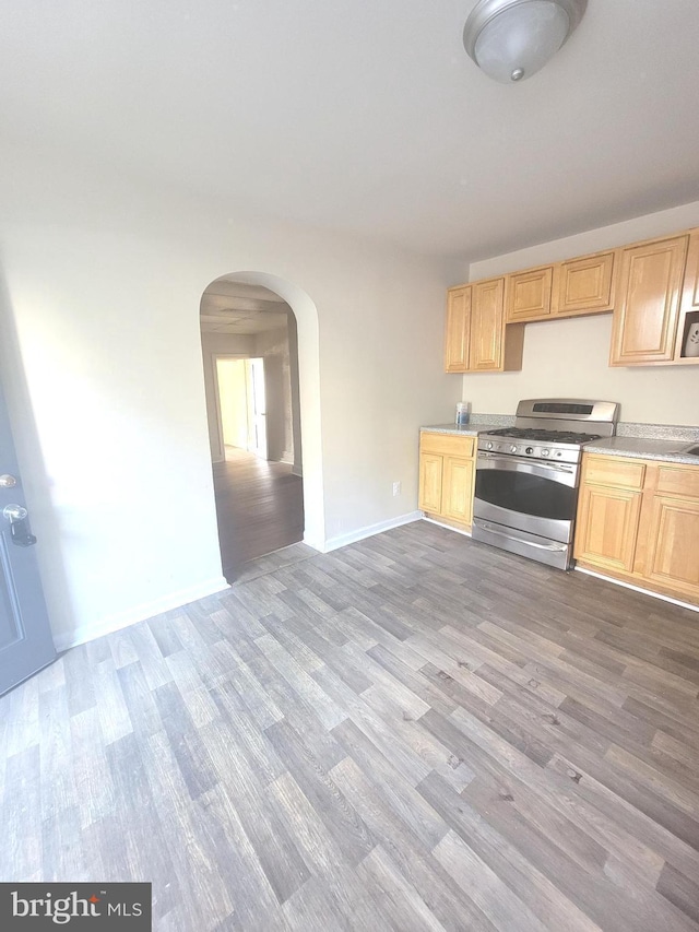 kitchen featuring arched walkways, light brown cabinetry, gas stove, and wood finished floors